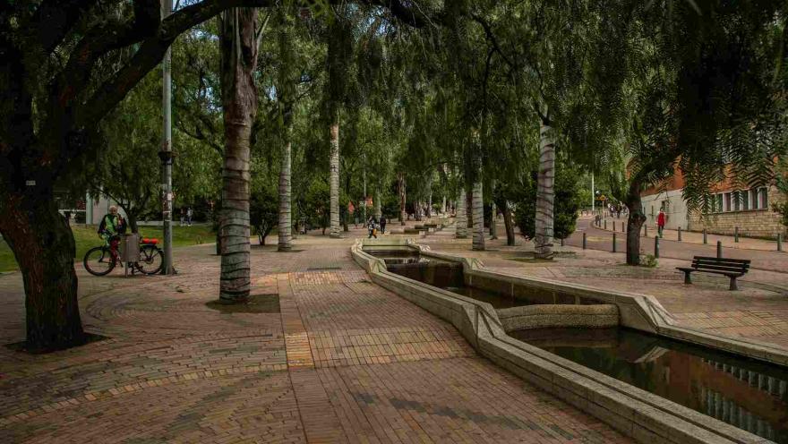 A promenade with a long fountain surrounded by trees. There are a few people nearby. 