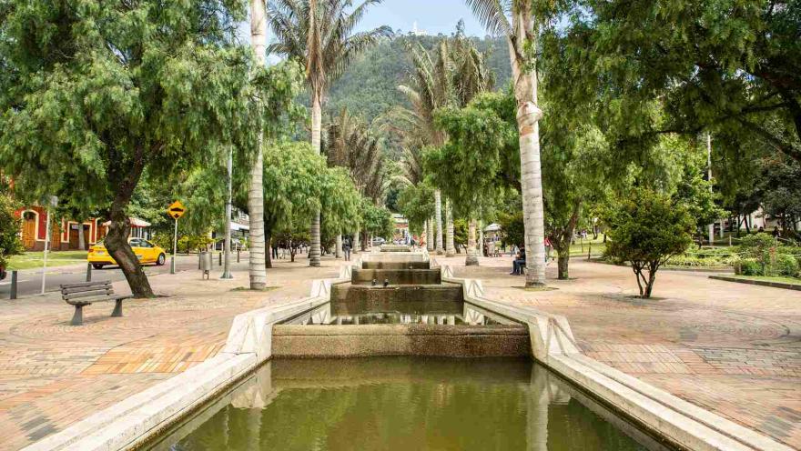 A promenade with a long fountain surrounded by trees. There is a taxi nearby.