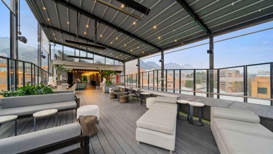 Una amplia terraza en la azotea con vistas a la ciudad y las montañas. Está amueblada con sofás y mesas, ideal para eventos o para relajarse al aire libre.