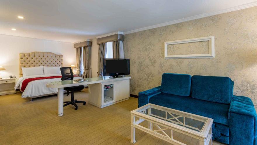  Espaciosa suite de hotel con cama king-size, sofá turquesa y escritorio. 