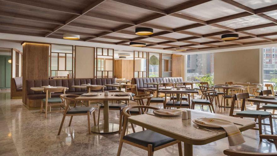 Restaurante luminoso con mesas de madera, asientos cómodos y techo enrejado.
