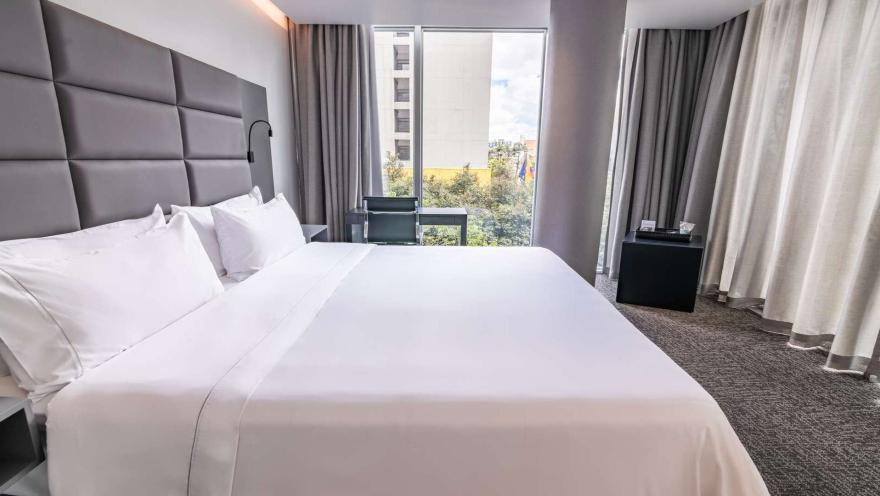 Habitación de hotel con dos camas dobles, cabeceras grises y amplios ventanales.