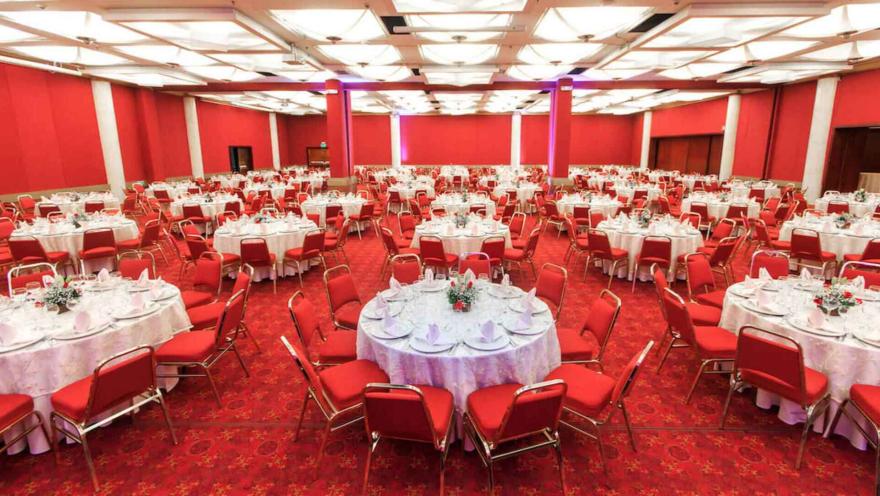 Gran salón de eventos con mesas redondas y sillas rojas. Ideal para banquetes o conferencias.