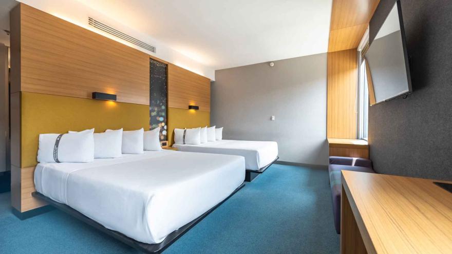  Una habitación de hotel Aloft con dos camas dobles, un banco junto a la ventana y una decoración moderna y colorida, ideal para familias o grupos.