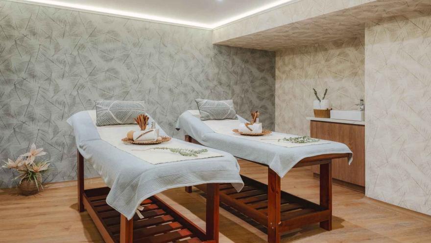 Sala de spa con dos camillas de masaje preparadas y decoración de hojas.