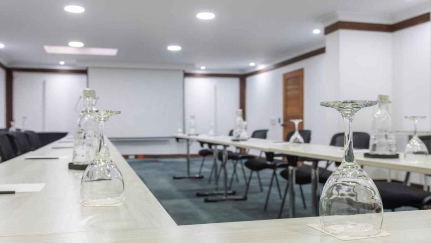 Sala de conferencias preparada con mesas largas y copas invertidas. 