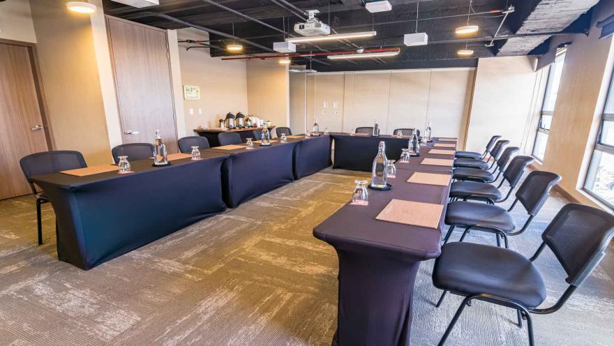 Sala de reuniones configurada en forma de U con mesas y sillas negras.