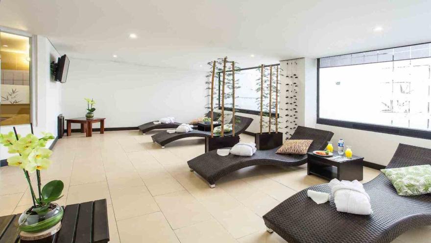 Un área de relajación tipo spa con varias tumbonas de mimbre, batas blancas y orquídeas decorativas. El espacio es luminoso y sereno.