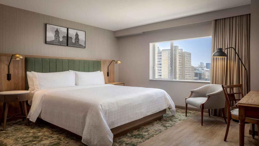 Habitación de hotel con cama king-size, cabecera verde y vista a la ciudad.