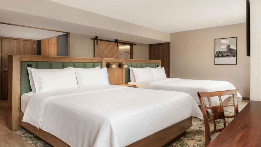  Habitación de hotel con dos camas dobles, cabeceras verdes y puerta corrediza.