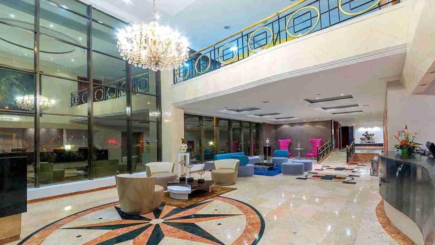  Un gran lobby de hotel con techos altos, un impresionante candelabro, grandes ventanales y una mezcla de mobiliario moderno y clásico.