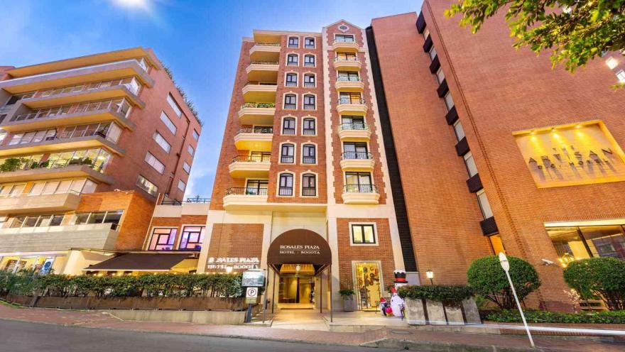 La fachada de un hotel de ladrillo con balcones, toldo en la entrada y el nombre "Rosales Plaza Hotel Bogota" claramente visible.