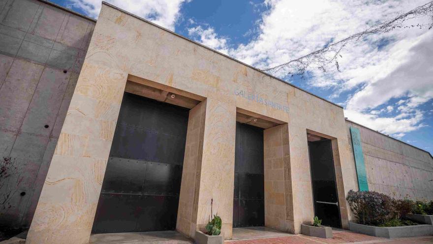 Fachada de edificación en piedra en la que destacan dos puertas altas y negras, parece que de metal, y una leyenda sobre la parte superior que dice: “GALERÍA SANTA FE”. 