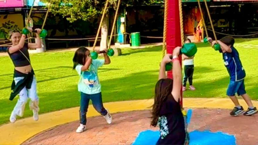 Niños cuelgan de unas cuerdas en un parque de atracciones.