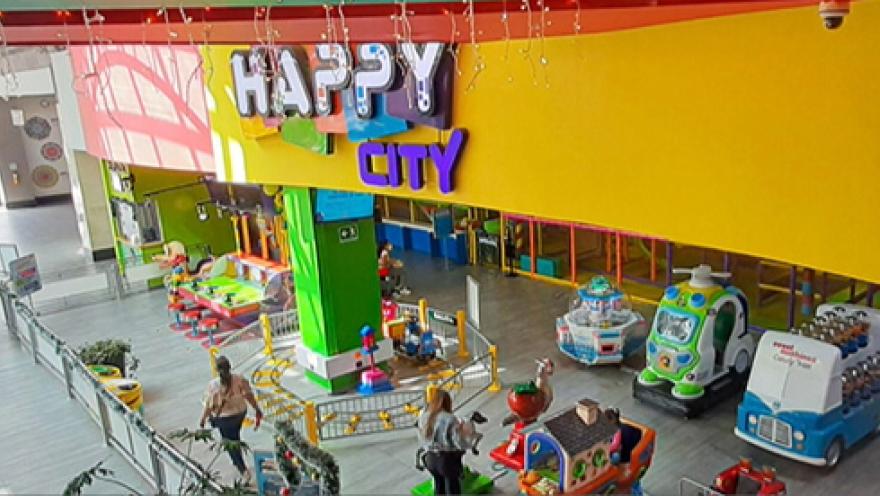 Salón visto desde arriba, en el que hay varias atraccciones mecánicas con coloridas figuras de animales y cosas. Destaca un aviso grande con una leyenda que dice: "Happy City".