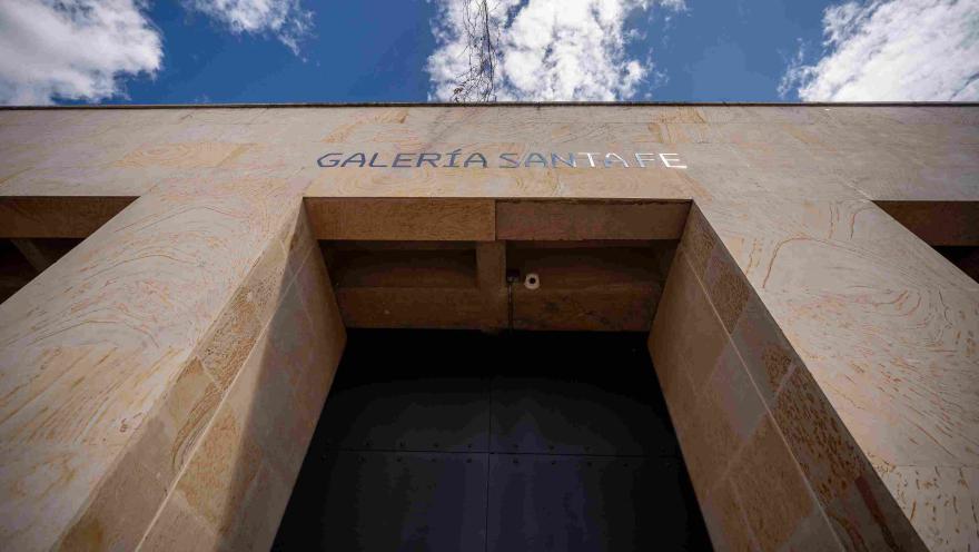 Plano de abajo hacia arriba de la fachada de edificación en piedra en la que destaca una puerta alta y negra, parece que de metal, y una leyenda sobre la parte superior que dice: “GALERÍA SANTA FE”. 