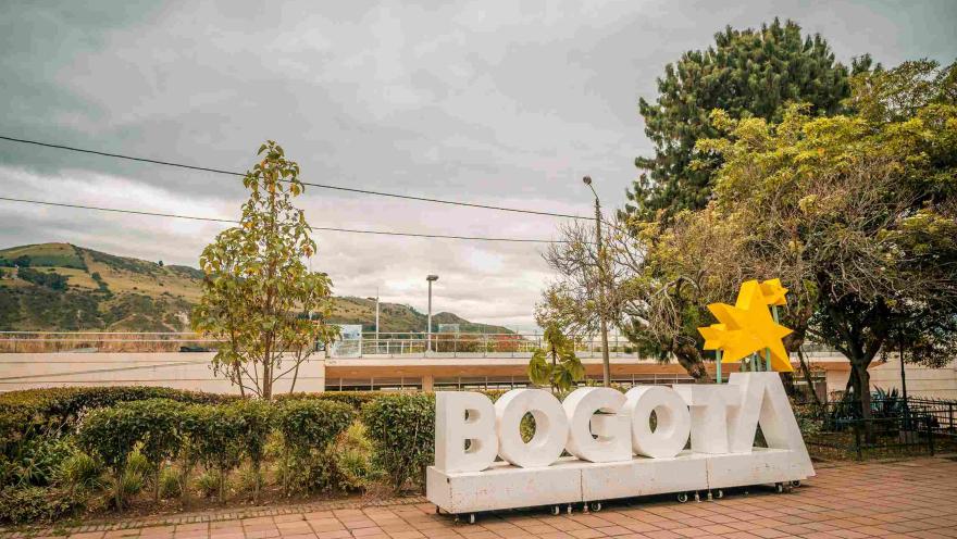 A large white sign with the word Bogotá, with yellow stars above the letter “A.” In the background, mountains can be seen.