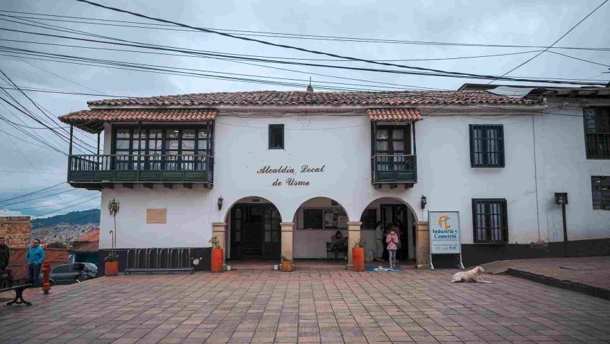 Facade of a two-story old white house, featuring a sign that reads: “Alcaldía Local de Usme.”