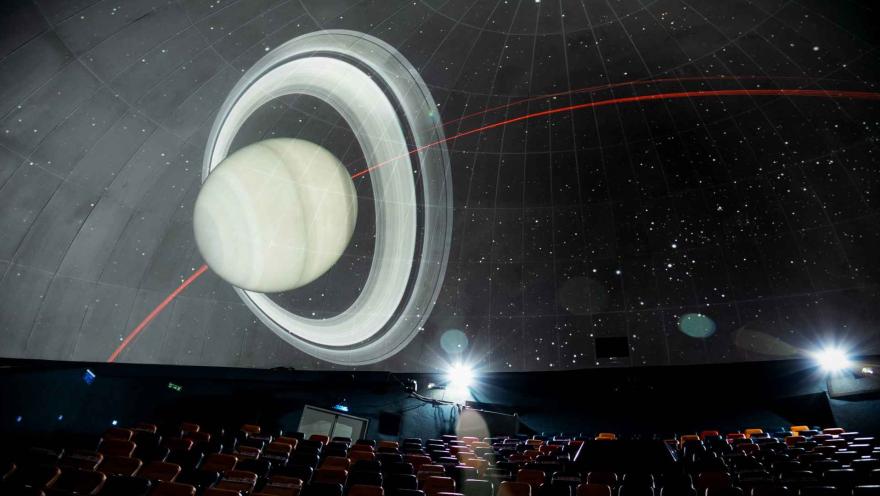 Salón interior que parece una sala de cine en la que se proyectan figuras como planetas y estrellas.