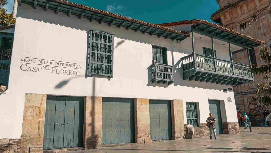 Fachada de casa antigua de estilo colonial con balcones y puertas de color verde. Resalta una leyenda en una de las paredes blancas, que dice: “Museo de la Independencia - Casa del Florero”.