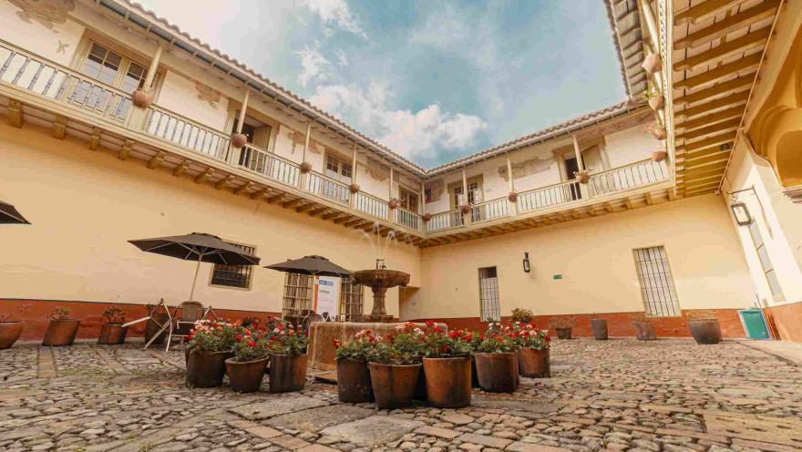 Interior de casona antigua en la que sobresalen balcones en el segundo piso. El primer piso es un patio grande y empedrado con una fuente de agua en la mitad.