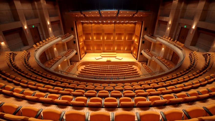  Interior de sala de teatro, visto de arriba hacia abajo, con varias filas de bancas color dorado.