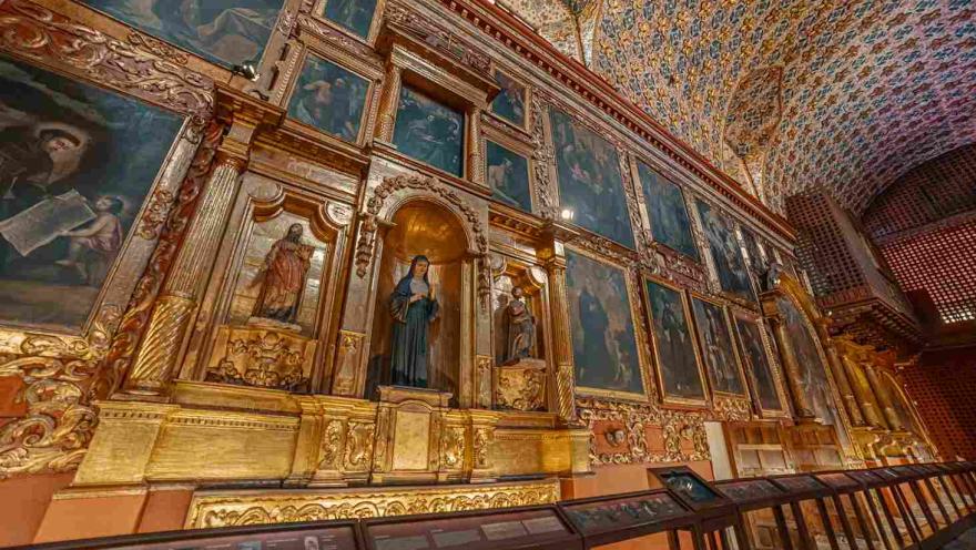 Pared abarrotada de cuadros y retablos.