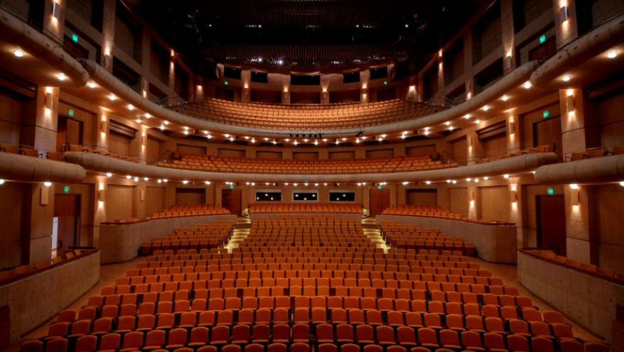 Interior de sala de teatro, visto de abajo hacia arriba, con varias filas de bancas color dorado.