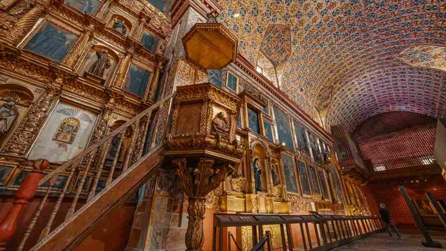 Púlpito en madera delante de una pared abarrotada por cuadros y retablos.