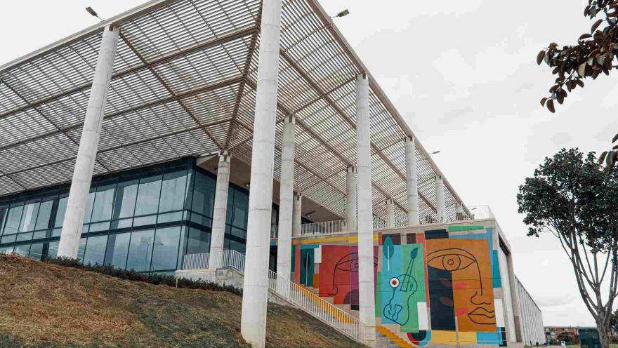 Gran estructura entre metal y vidrio. Hay una pared con imágenes de rostros de colores.
