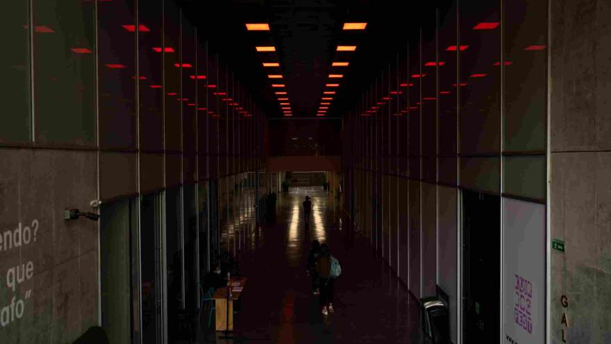 Largo pasillo interior oscuro y con varias oficinas a lado y lado. Algunas personas caminan alrededor.