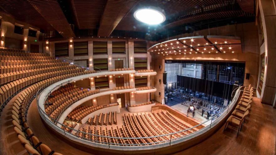 Interior de sala de teatro, visto de lado, con varias filas de bancas color dorado en forma de espiral.