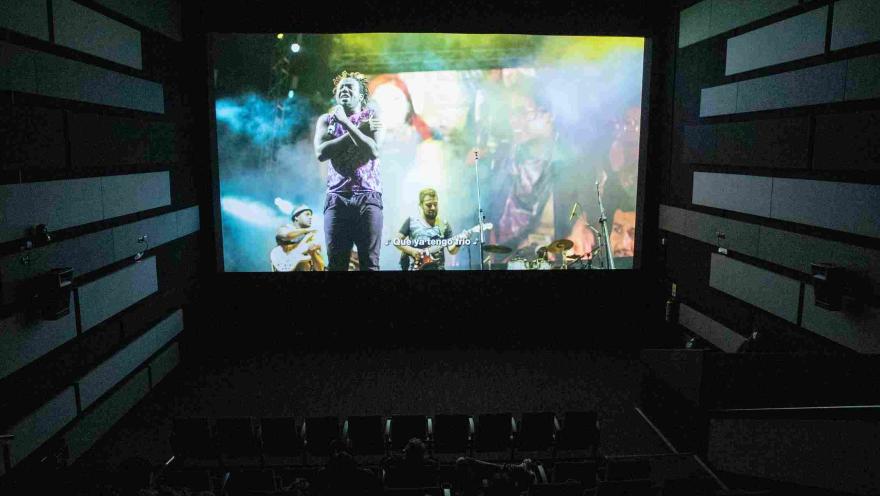 Interior de sala de cine en la que se proyecta una película en la que se observa a una banda musical.