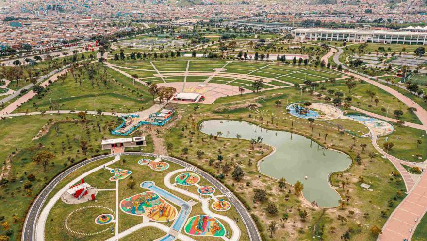 Plano general visto desde arriba de un parque gigantesco donde hay amplias zonas verdes, un parque infantil y un gran lago.