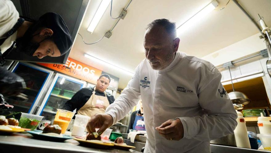 Un chef experimentado, en un uniforme blanco, emplatando con precisión un pequeño plato en una cocina.