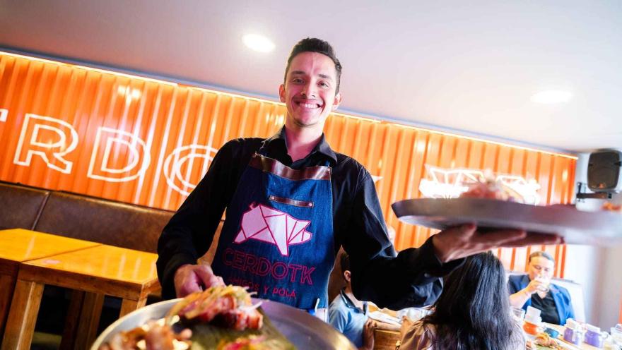 Un camarero sonriente en un restaurante moderno, sirviendo dos platos con chicharrón. 