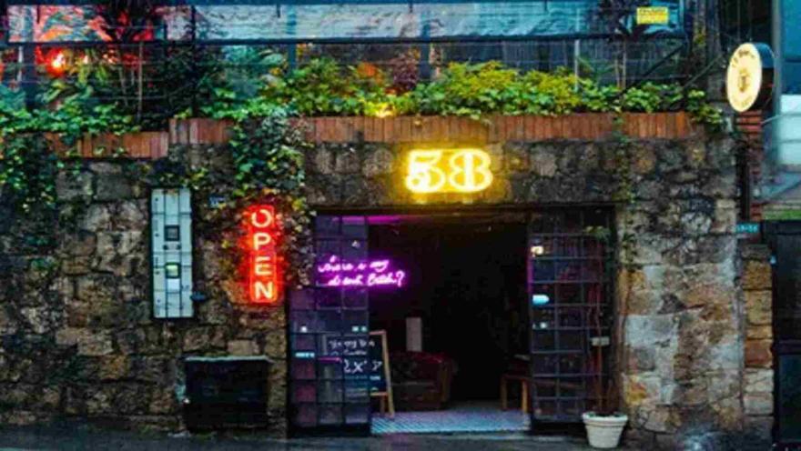  Entrada de un bar/restaurante con paredes de piedra, plantas y letreros de neón "OPEN" y "58". 