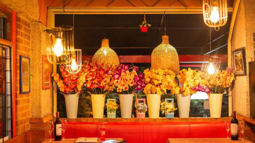 Un interior de restaurante decorado con exuberantes arreglos florales y lámparas colgantes, creando un ambiente vibrante. 