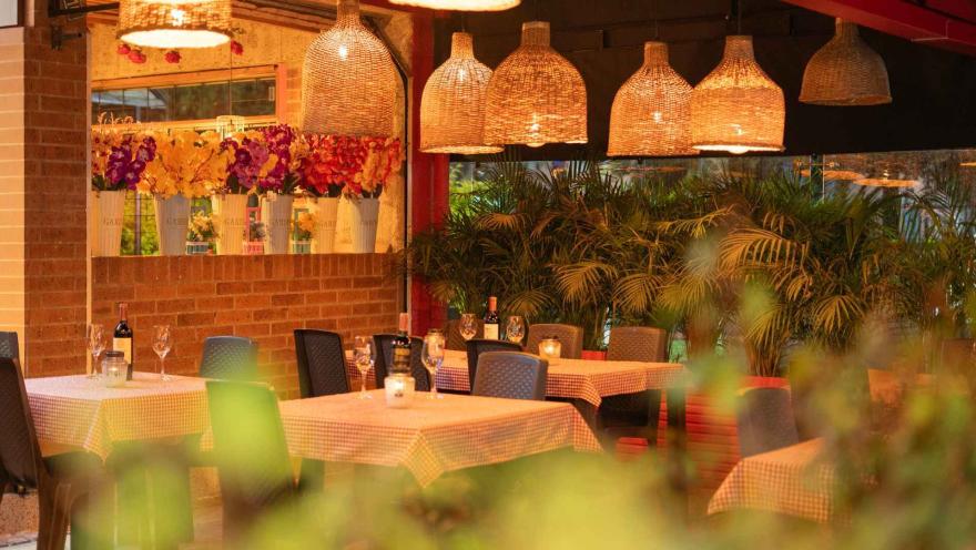  Mesas preparadas para cenar en un ambiente de restaurante con decoración cálida, luces y vegetación. al.