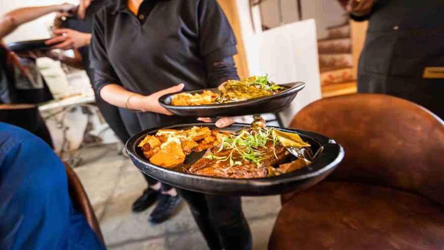Una persona sirviendo dos platos con comidas gourmet, adornados con hierbas y acompañamientos. 