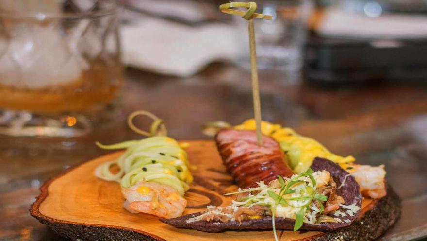 Tabla de madera con una selección de variados y coloridos aperitivos gourmet y un cóctel. 