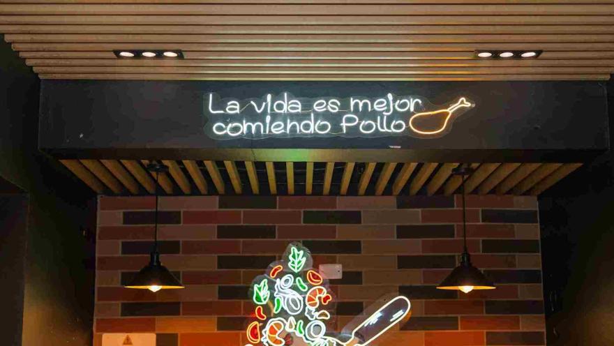 Un letrero de neón con la frase "La vida es mejor comiendo pollo" ilumina el techo de madera del restaurante.