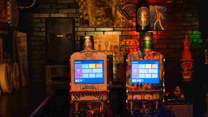 Dos máquinas recreativas digitales con temática de Jack Daniel's y Los Simpson en un bar.