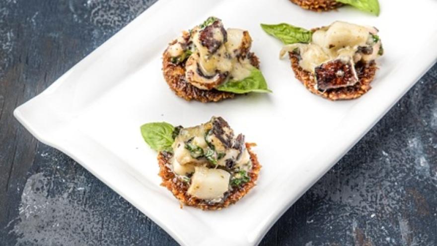 Canapés individuales elegantemente presentados con mariscos y hojas de albahaca sobre una bandeja blanca alargada. 