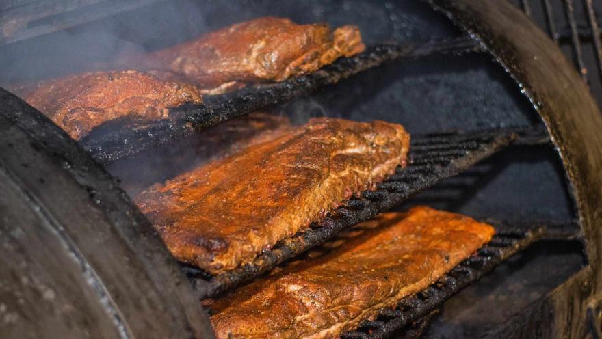 Costillas de cerdo asándose lentamente en una parrilla humeante, mostrando su delicioso ahumado. 