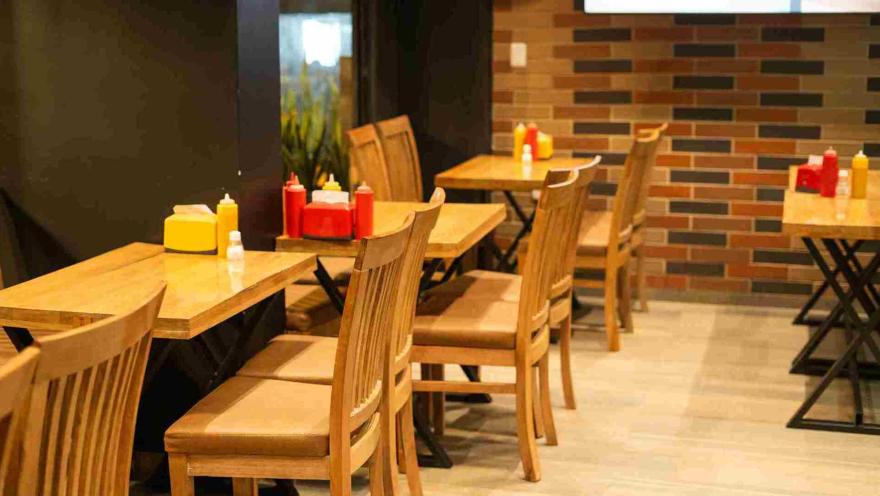 Vista de varias mesas y sillas de madera dispuestas en el interior del restaurante, listas para los clientes.