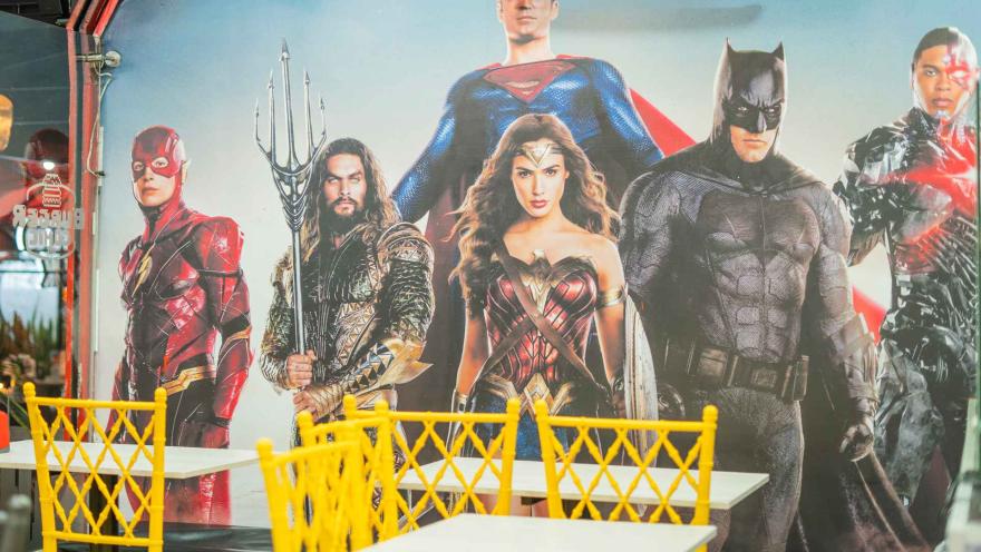 Un mural de pared grande muestra a los personajes de la Liga de la Justicia. Sillas amarillas están colocadas enfrente.