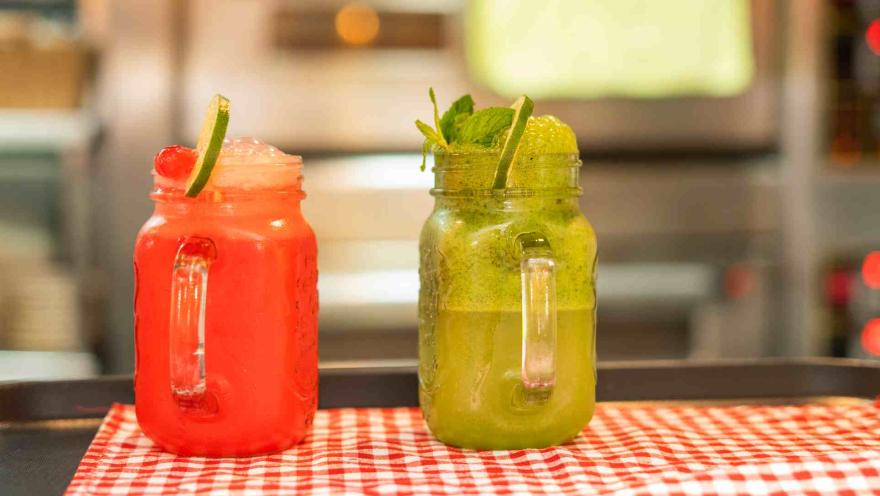 Primer plano de dos bebidas refrescantes de colores vibrantes servidas en tarros de cristal decorados.