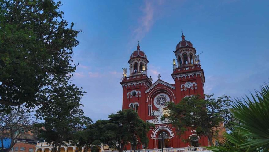The church facade, painted red, at sunset. Its two Greco-Roman towers, shaped like arches and flanked by angel figures, are particularly striking.