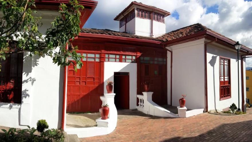  Fachada de casa estilo colonial donde las paredes son blancas y las puertas y ventanas rojas.
